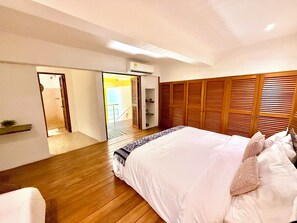 A bedroom with a wooden floor, a bed with white bedding, a wooden wardrobe, and a door leading to a bathroom. - Calamari Homes - El Porvenir 205 - Walled City (Cartagena de Indias)