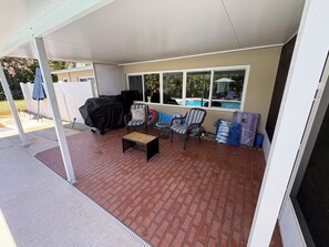 A covered patio area with a barbecue grill, outdoor furniture, and a view of a swimming pool. - Tranquil Riverfront Retreat with Private Pool & Screened Lanai (Jensen Beach)