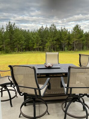 An outdoor patio with a table and chairs, surrounded by a grassy area and a forest.