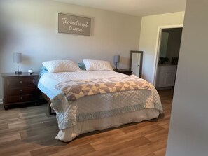 A bedroom with a bed, nightstands, a dresser, a mirror, and a wall sign.