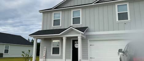 A two-story residential building with a garage, a front porch, and a welcome sign.