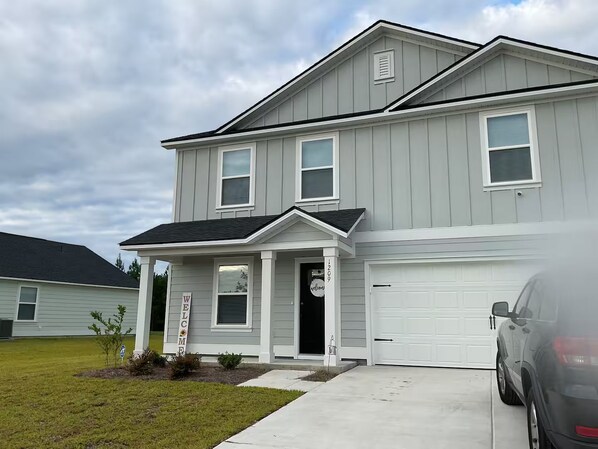 A two-story residential building with a garage, a front porch, and a welcome sign.