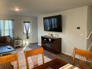 A living room with a flat-screen TV, a dining table with chairs, a sofa, and a small side table.