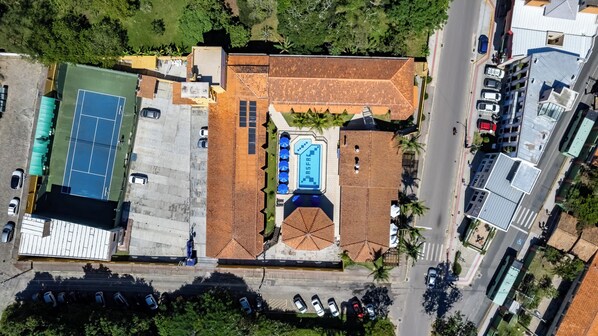 An aerial view of a property with a swimming pool, tennis court, and multiple parking spaces.