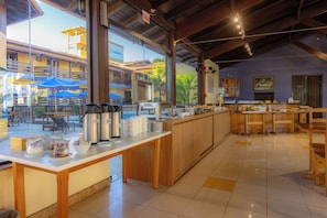 A breakfast bar with coffee makers, a buffet with various food items, and a view of the outdoor seating area.