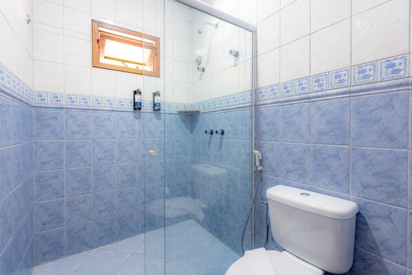 A bathroom with a glass shower enclosure, a toilet, and a small window above the shower.