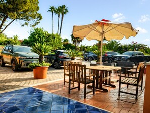 Un patio al aire libre con suelo de baldosas, muebles de madera y una gran sombrilla que da sombra.