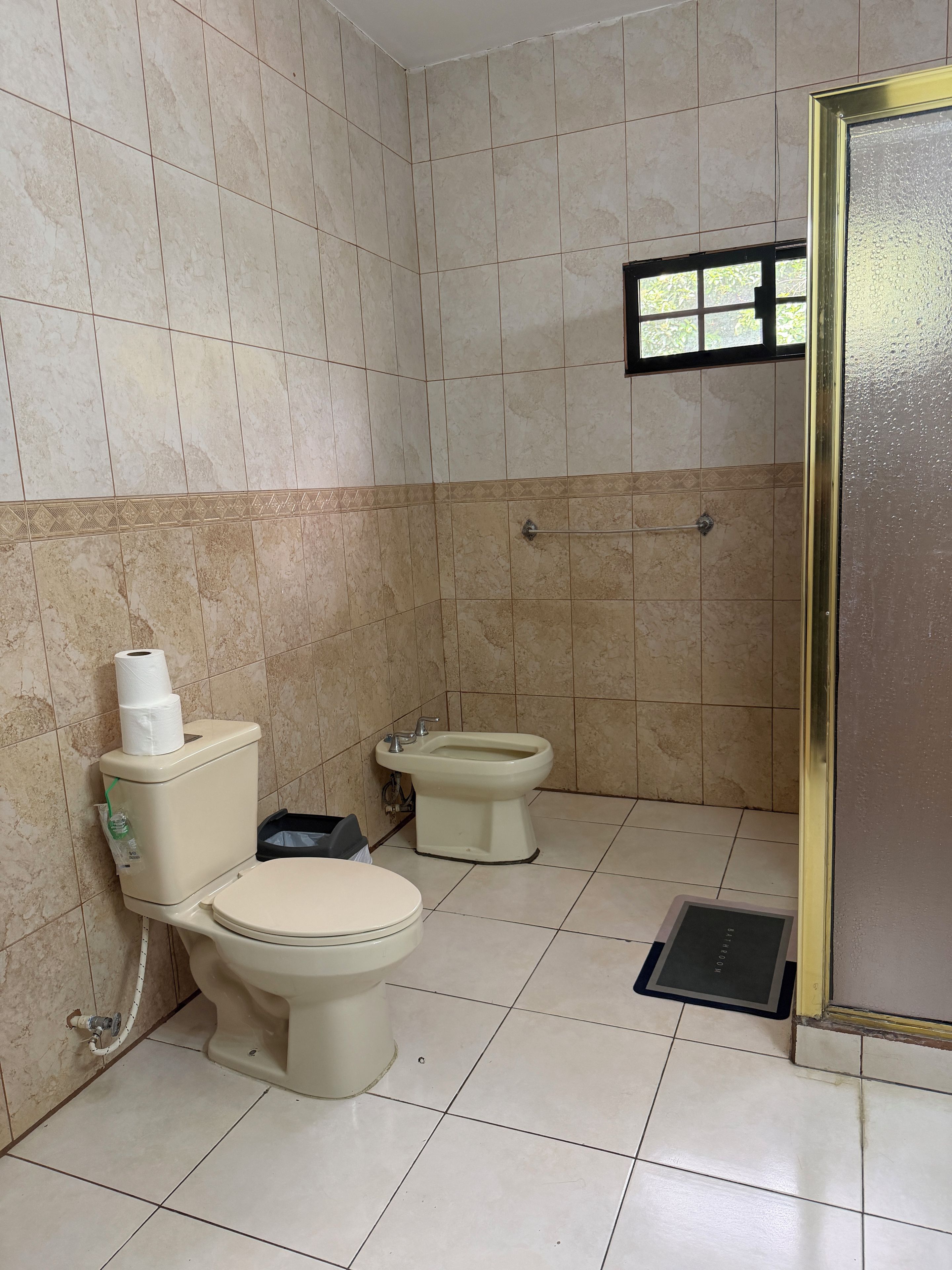 A bathroom with two toilets, a bidet, and a window.