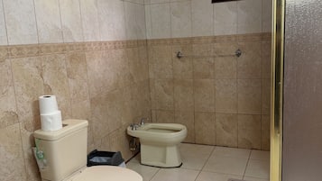 A bathroom with two toilets, a bidet, and a window.