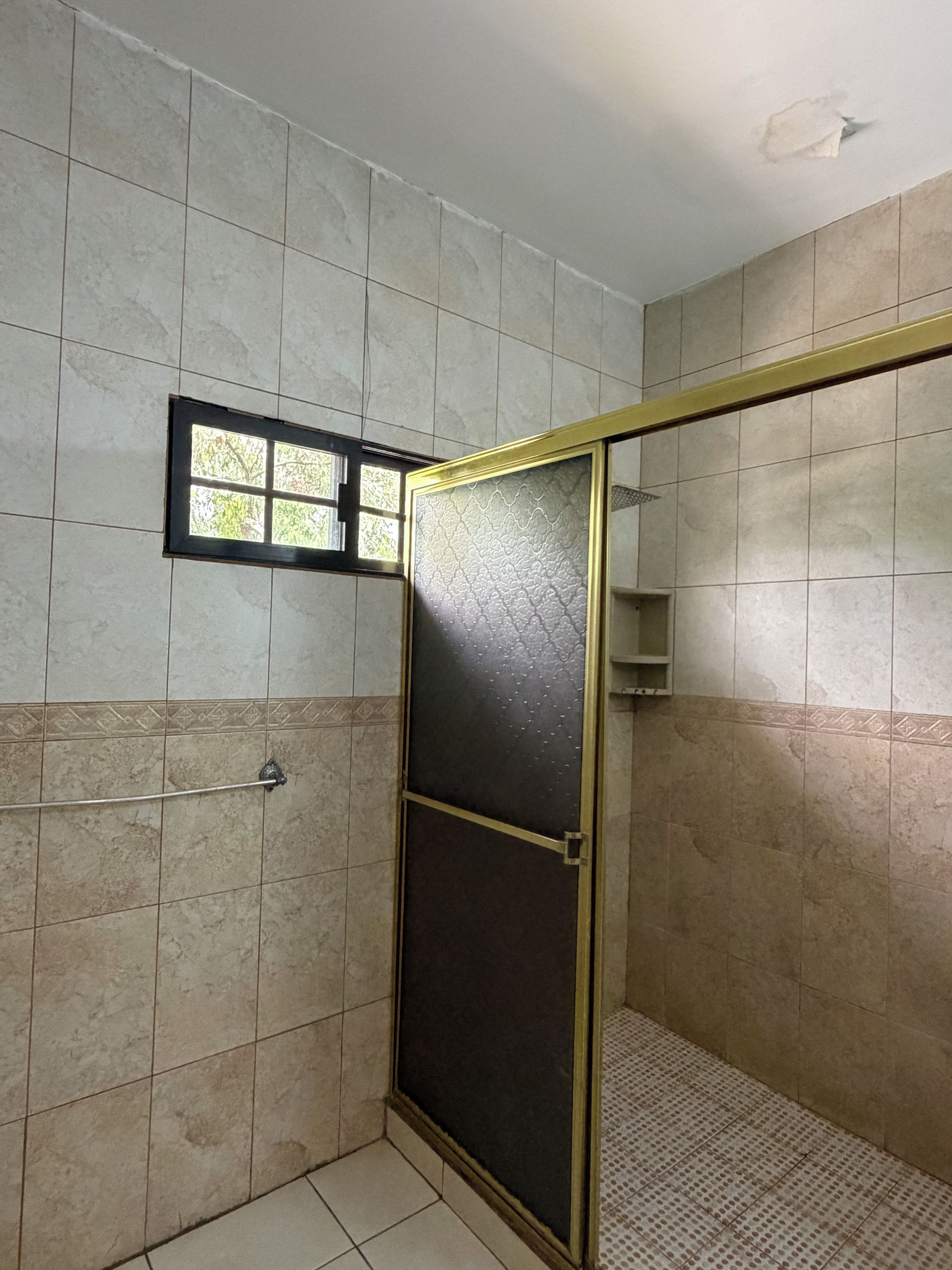 A bathroom with a shower area, tiled walls, and a window.