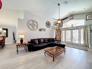 A modern living room with a sectional sofa, a glass coffee table, and decorative wall art. - 4BR Villa Near Disney w/ Game Room & Private Pool (Kissimmee)