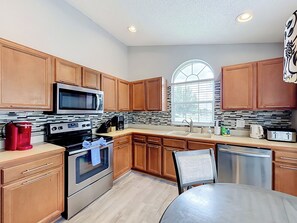 A modern kitchen with wooden cabinets, stainless steel appliances, a large window, and a tiled backsplash. - 4BR Villa Near Disney w/ Game Room & Private Pool (Kissimmee)