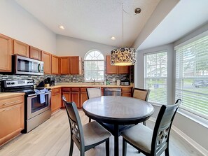 A modern kitchen with wooden cabinets, stainless steel appliances, a round dining table, and a large window with blinds. - 4BR Villa Near Disney w/ Game Room & Private Pool (Kissimmee)