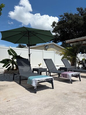 Un espace aménagé au bord de la piscine, avec des chaises longues, un grand parasol et une plante en pot.
