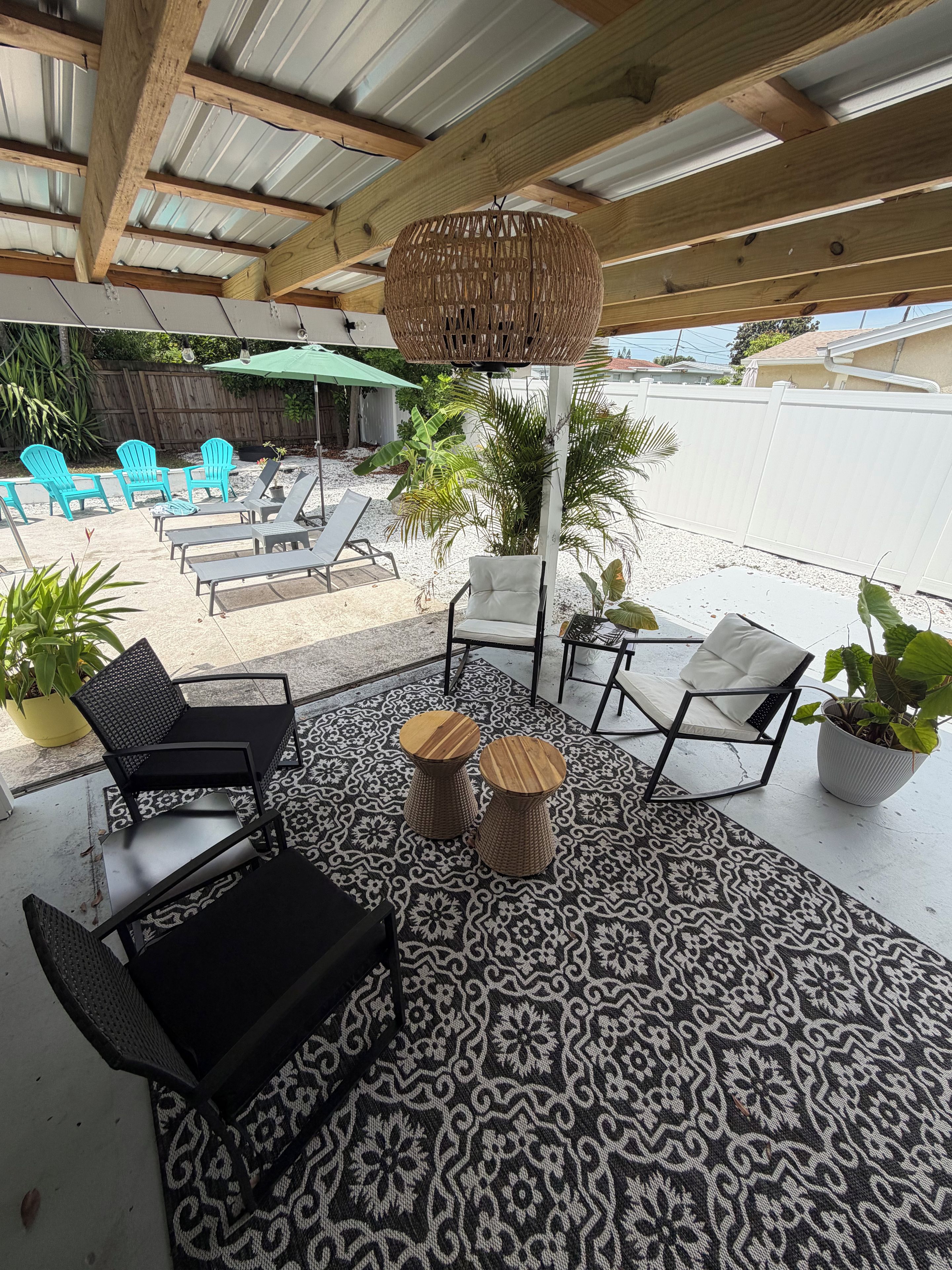 A covered outdoor seating area with lounge chairs and a patterned rug.