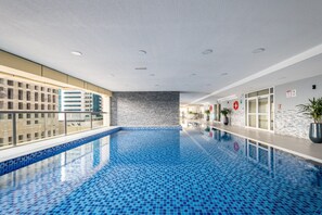 A modern indoor swimming pool with a blue tiled floor, a glass barrier on one side, and a brick wall on the other. - Chic 1BR Retreat High Floor Dubai Marina (Dubai)