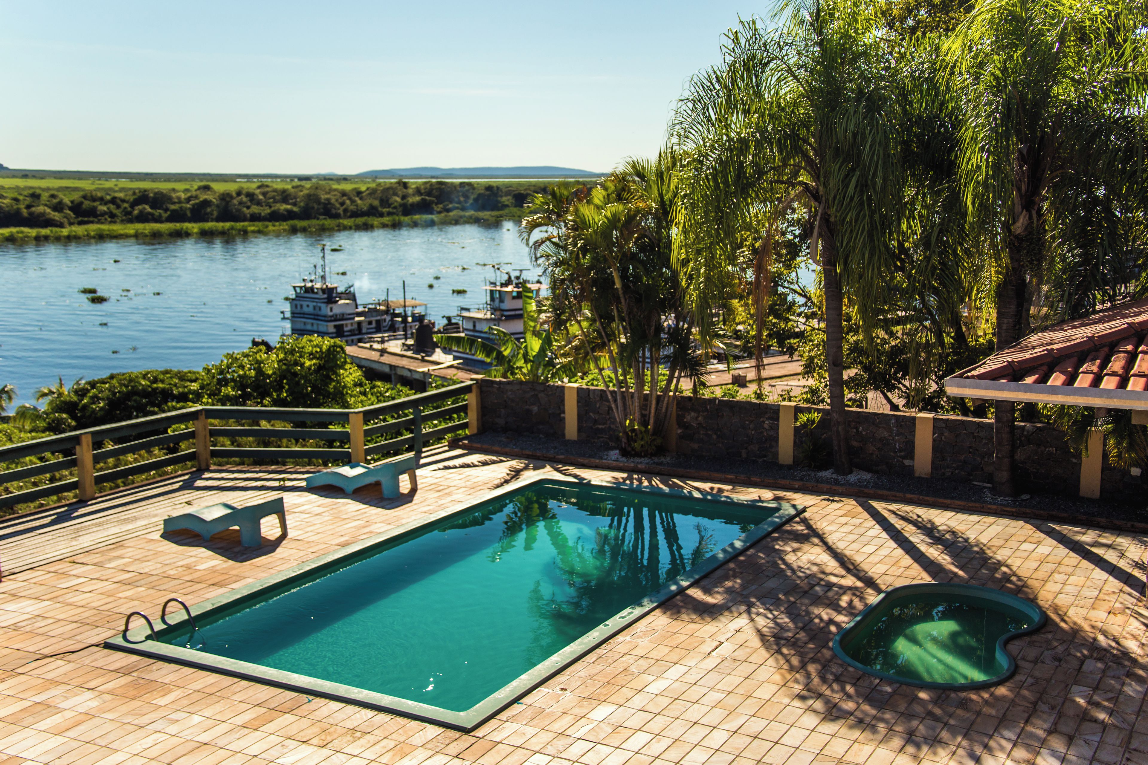 A swimming pool with a view of a river and boats, surrounded by a wooden deck and greenery.