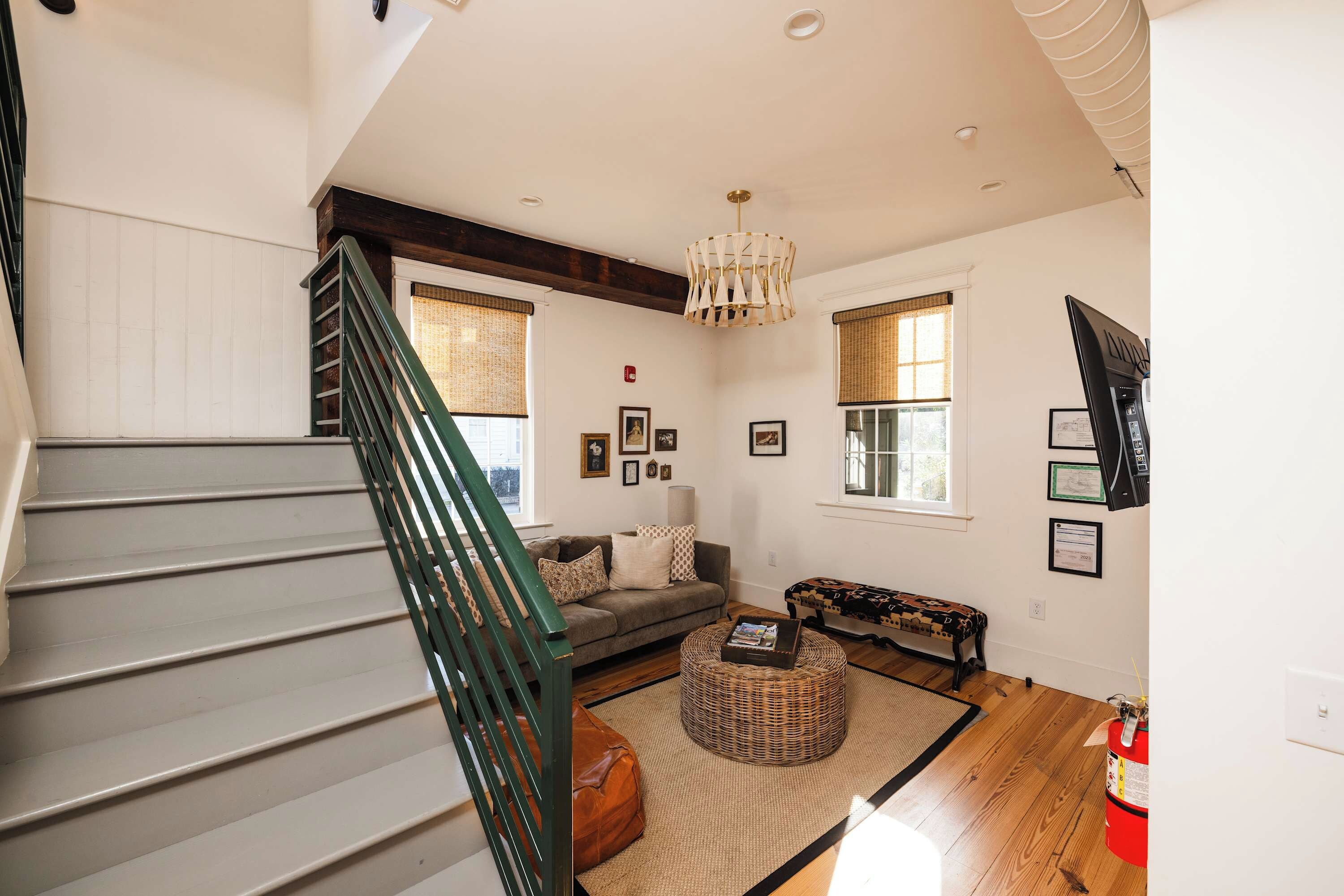 A staircase with a green handrail leading to a living room with a sofa, a patterned ottoman, and a bench.