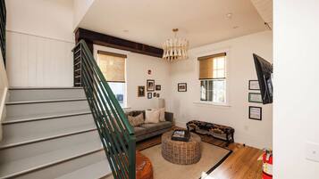 A staircase with a green handrail leading to a living room with a sofa, a patterned ottoman, and a bench.