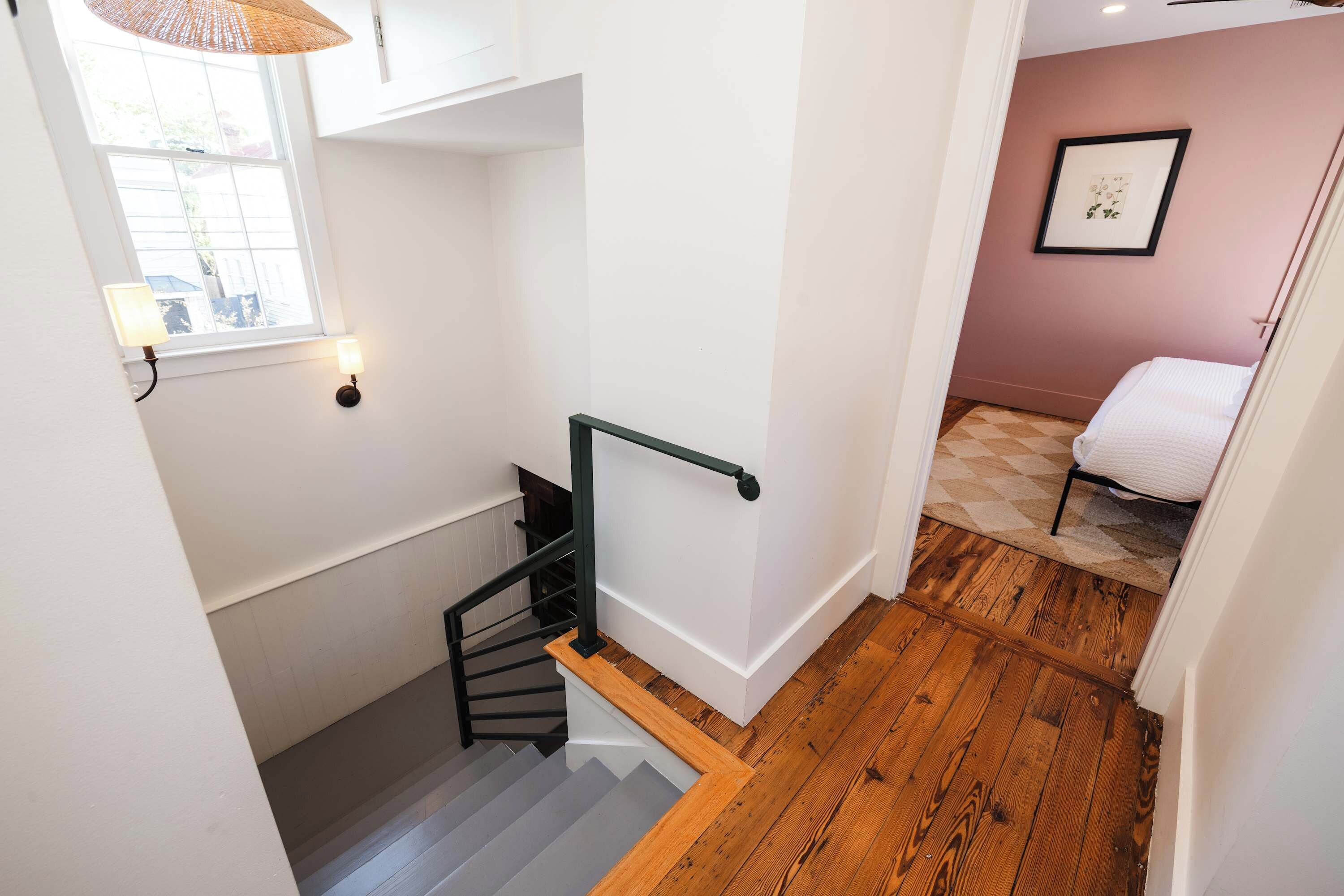 Un escalier avec une main courante en bois et une rampe en métal noir, menant à une pièce où se trouvent un lit et un tableau encadré au mur.