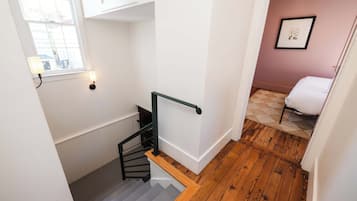 A staircase with a wooden handrail and a black metal railing, leading to a room with a bed and a framed picture on the wall.