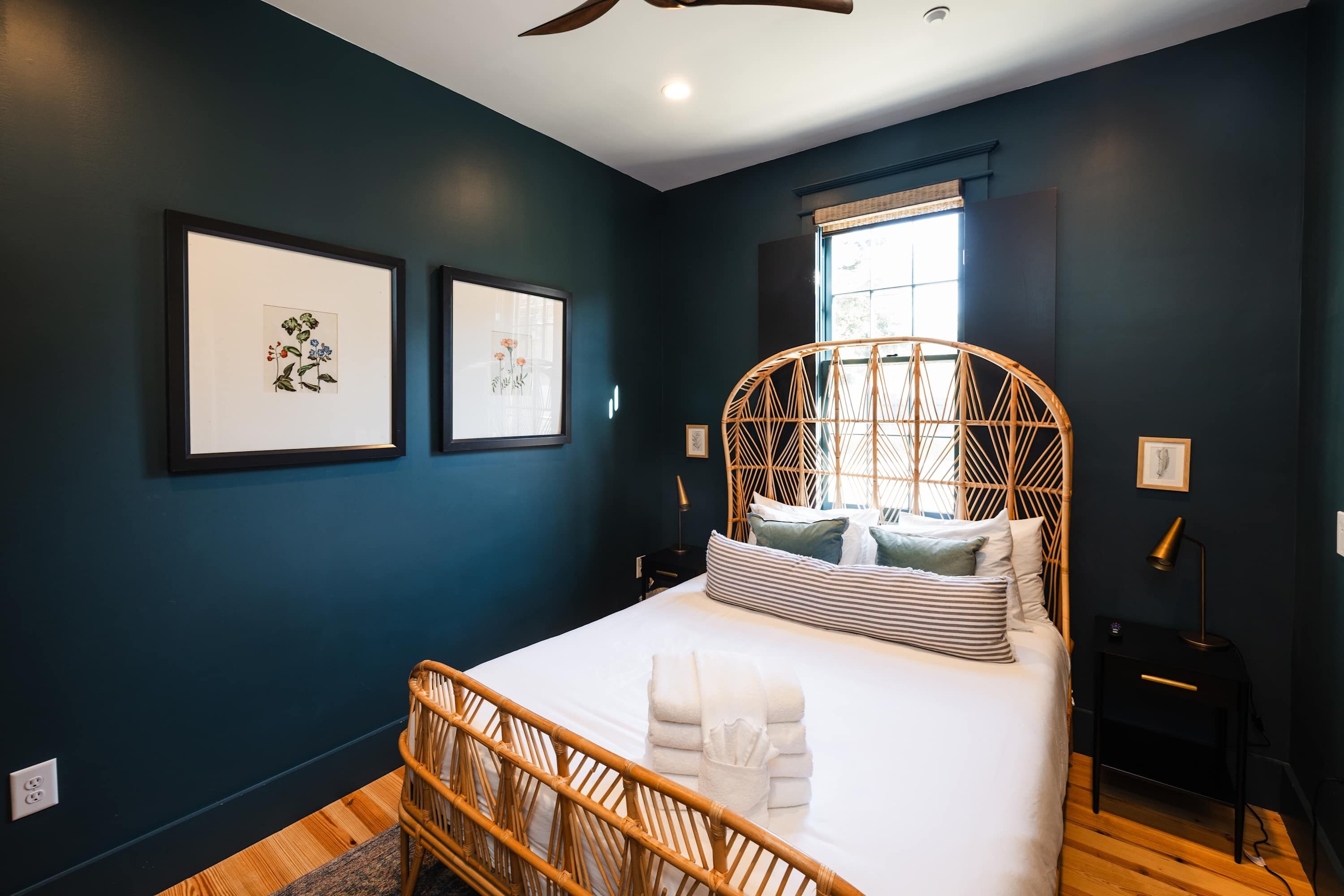 A bedroom with a bed, a window, and two framed botanical prints on the wall.
