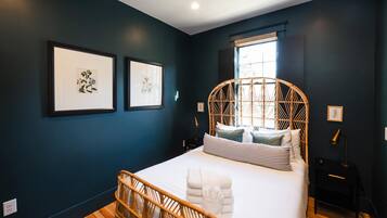 A bedroom with a bed, a window, and two framed botanical prints on the wall.