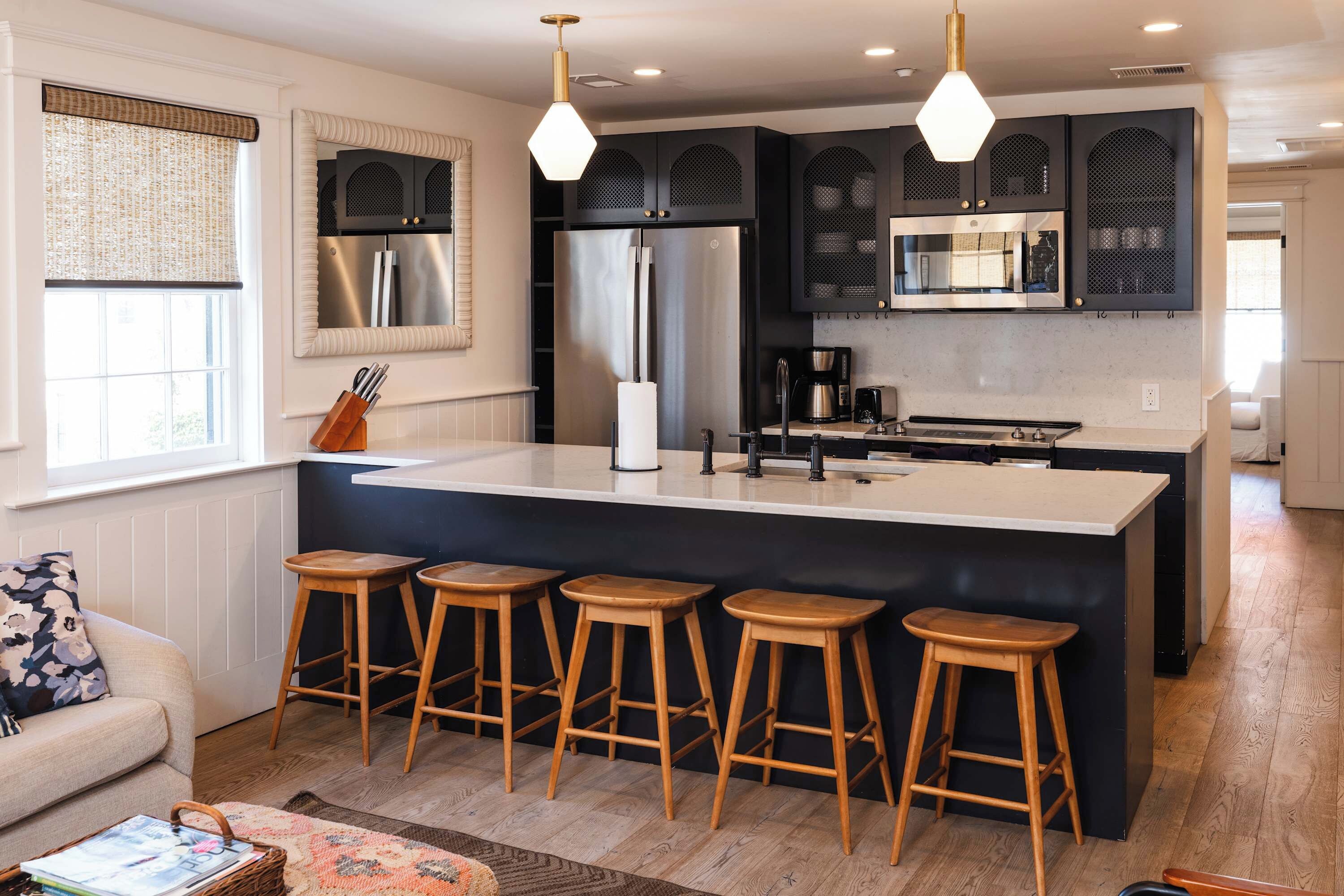 A modern kitchen with a central island, bar stools, stainless steel appliances, and pendant lighting.