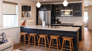 A modern kitchen with a central island, bar stools, stainless steel appliances, and pendant lighting.