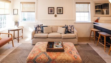 A living room with a sofa, a coffee table, a side table, and a kitchen area with a counter and stools.