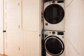 A laundry room with two stacked front-loading washing machines and a white door. - Downtown 3bd Retreat, Newly Updated & Bright! (Charleston)