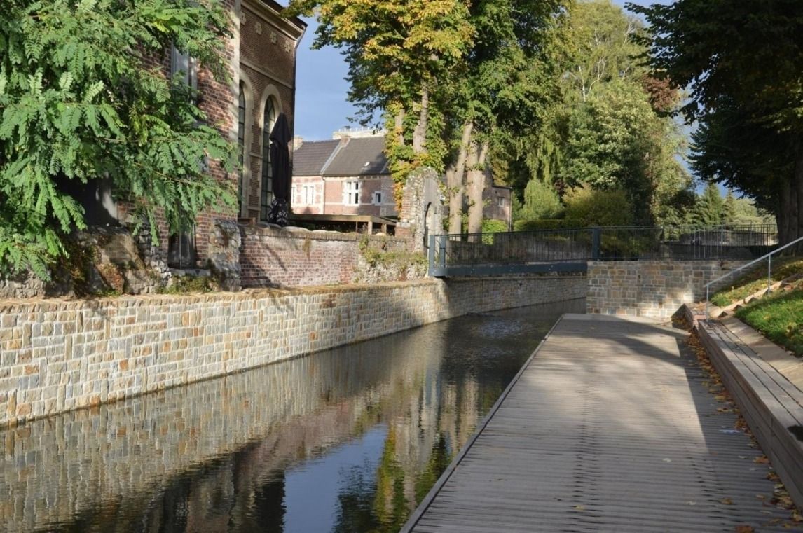 Un canal amb una passera de fusta, parets de pedra i un edifici amb façana de maó.
