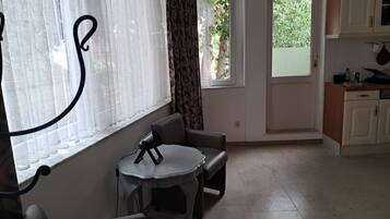A room with a dining table, a sofa, a window with curtains, and a view of the outdoors.