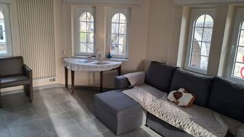 Una sala de estar con un sofá gris, una mesita redonda y dos ventanas con arcos.