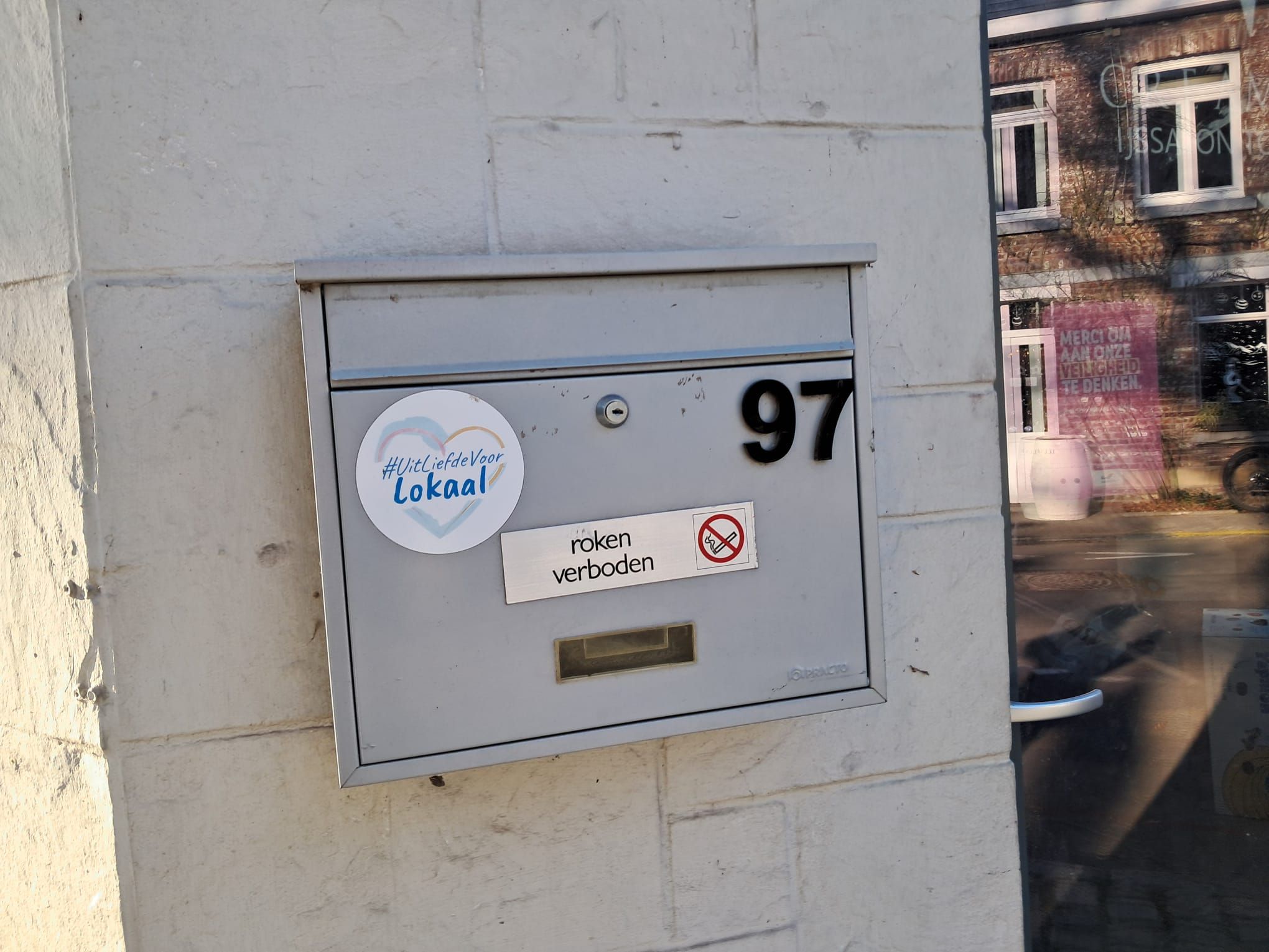 Une boîte aux lettres portant le numéro 97, un autocollant avec un cœur et un texte, et un panneau indiquant qu'il est interdit de fumer.