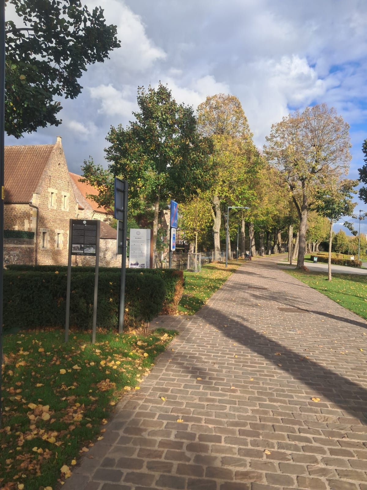 A paved pathway lined with trees and a brick building with a traditional roof.