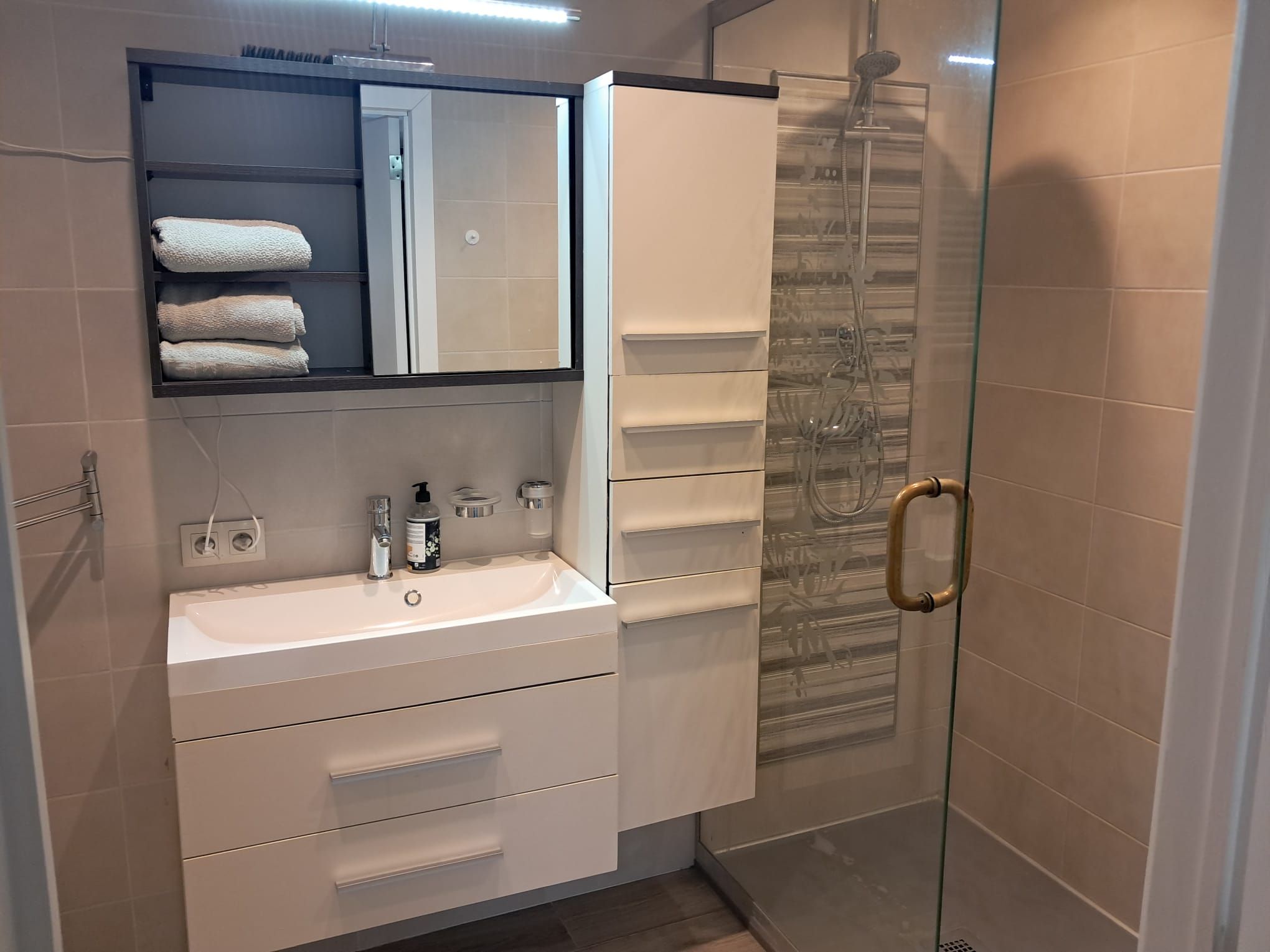 A modern bathroom with a white sink, a mirror, a towel rack, and a glass shower enclosure.