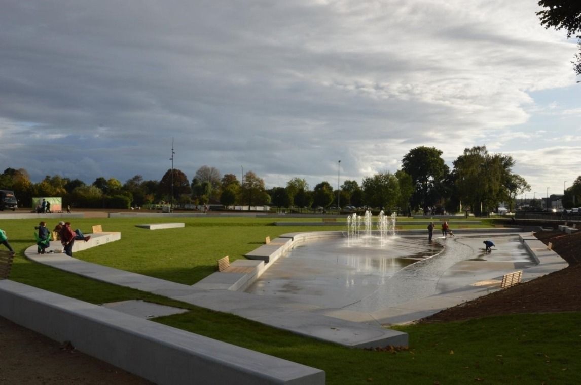 Ein Park mit einem Brunnen, Rasenflächen und einem gepflasterten Weg.