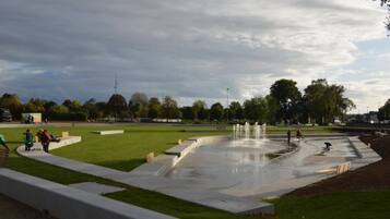 Ein Park mit einem Brunnen, Rasenflächen und einem gepflasterten Weg.