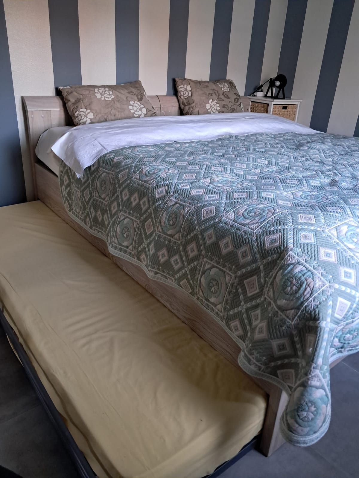 Una cama con colcha estampada, un banco y una mesita de noche con lámpara.