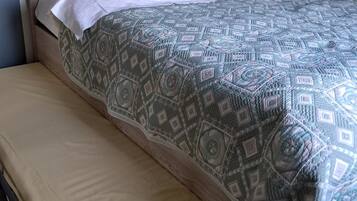 Una cama con colcha estampada, un banco y una mesita de noche con lámpara.