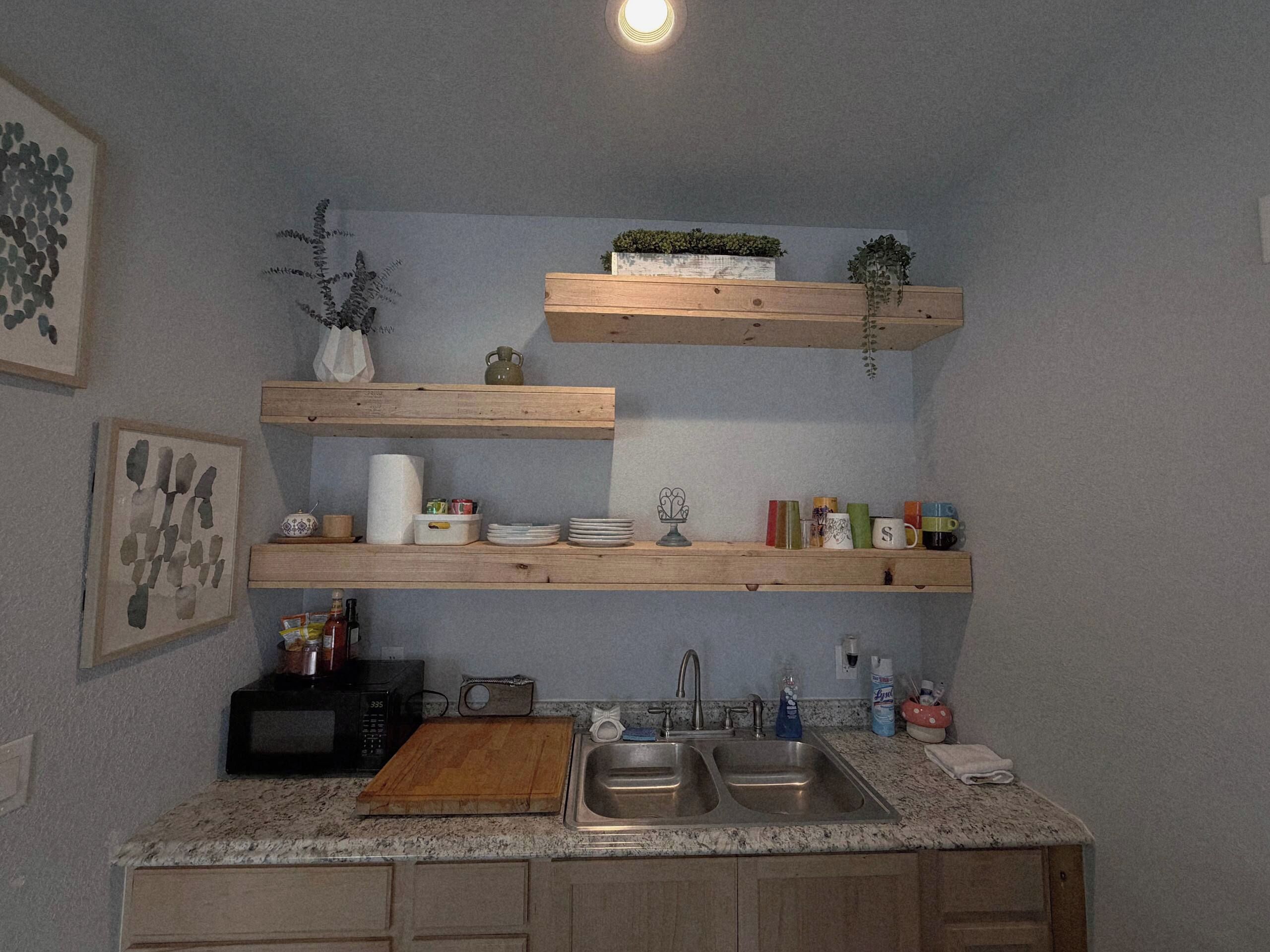 A kitchen with wooden shelves, a sink, and various kitchen items.