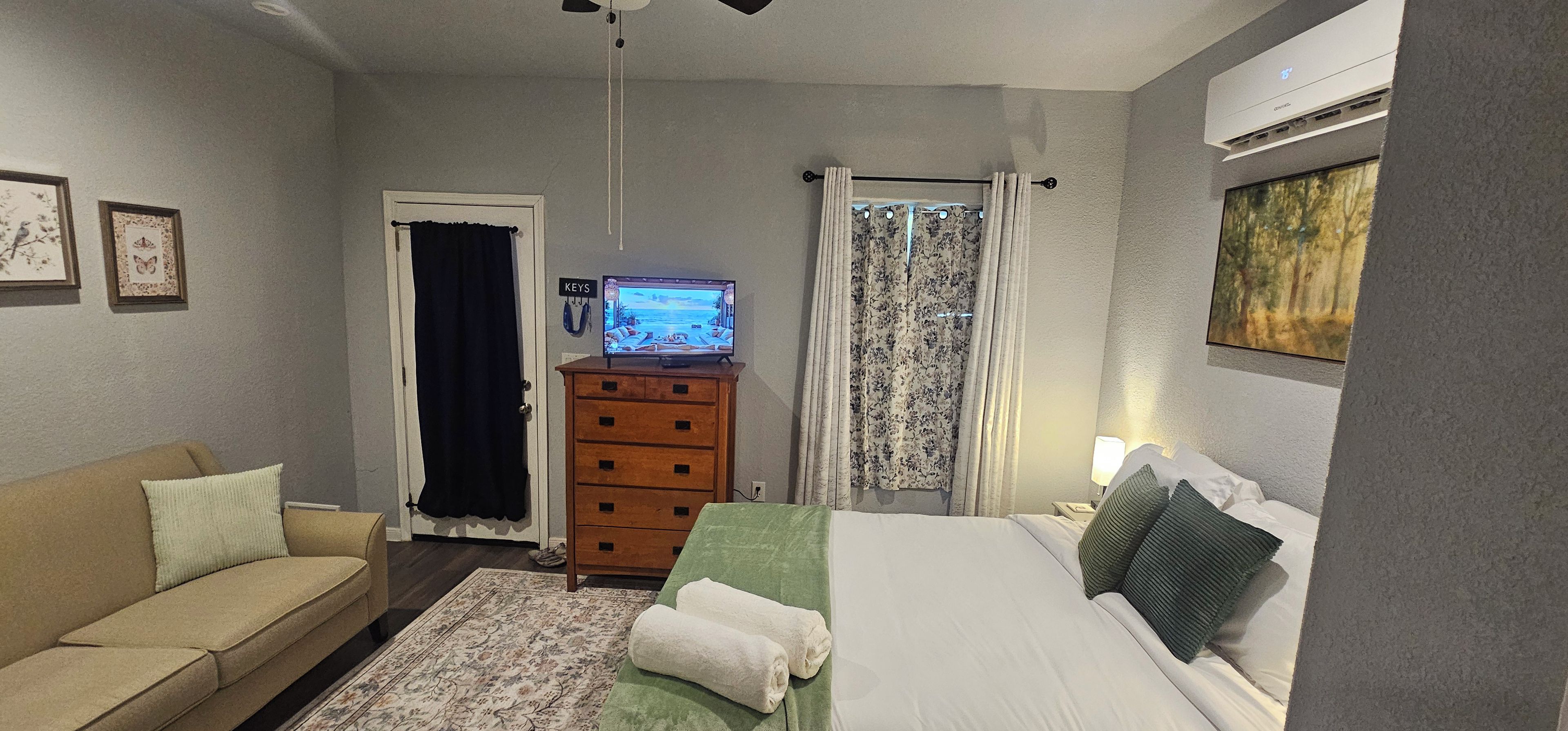 A bedroom with a bed, a dresser, a television, and a couch.