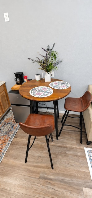 A dining area with a wooden table, two chairs, a coffee maker, a potted plant, and a patterned rug. - The Cozy Cardinal Studio (Bastrop)