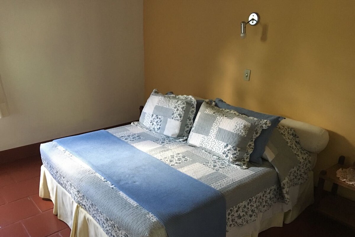 Un llit amb un llençol i coixins estampats en blau i blanc, un rellotge de paret i una taula petita amb un objecte decoratiu.