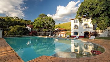 A swimming pool with lounge chairs, surrounded by a white building with yellow trim and a red roof.