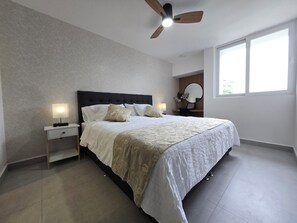 Ein Schlafzimmer mit einem Bett, Nachttischen, einem Deckenventilator und einem Fenster.