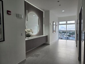 Ein moderner Flur mit einer Rezeption, einem großen Spiegel und Blick auf die Stadt durch große Fenster.