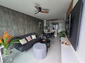 A modern living room with a black sofa, round coffee table, and a grey ottoman. A ceiling fan is visible above. - A beautiful new apartment in Uruka Point, San Jose. Great location! (San José)