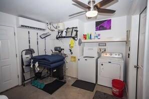 Un lavadero con ventilador de techo, lavadora, secadora y diversos productos de limpieza.